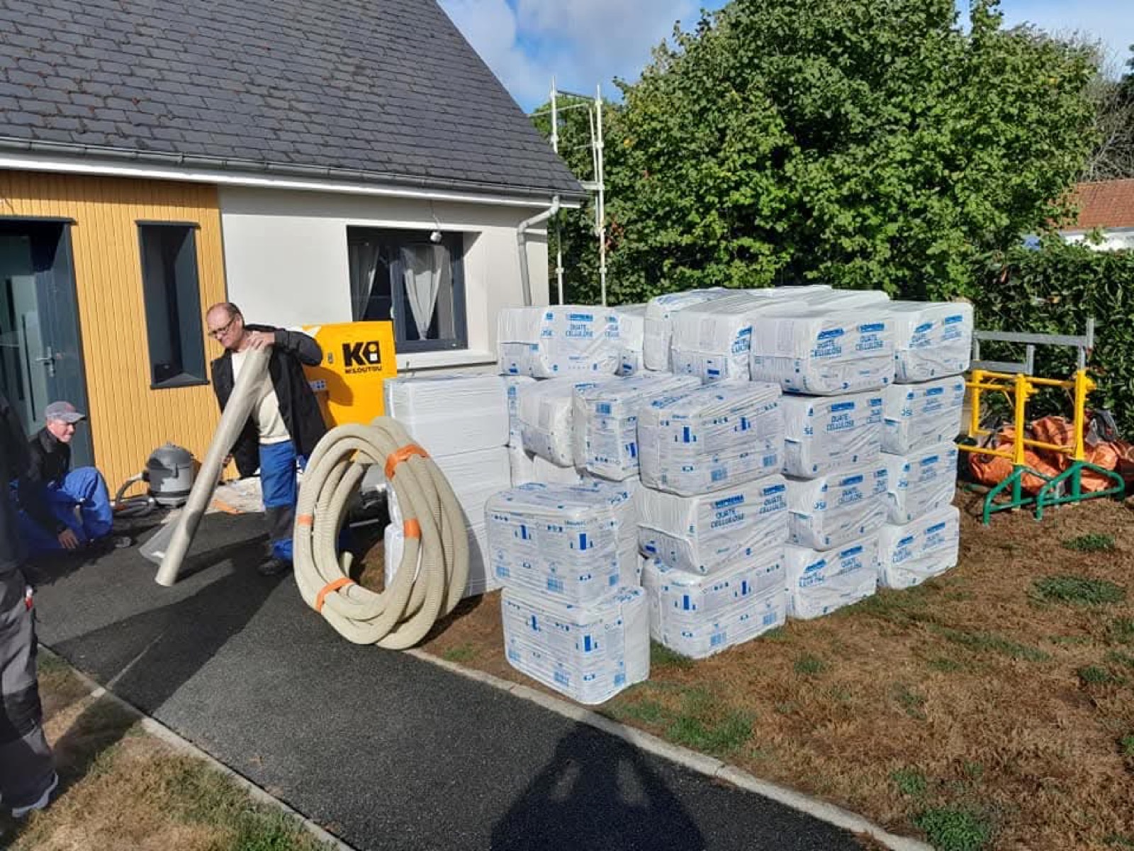 Technicien Dagicour chargeant la machine de soufflage de ouate de cellulose devant un pavillon, isolation de combles perdus en Seine-Maritime