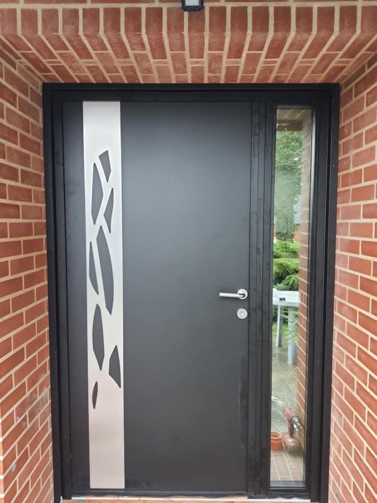 Porte d'entrée aluminium anthracite avec bande décorative géométrique et vitrage latéral, encadrement briques — Dagicour Normandie