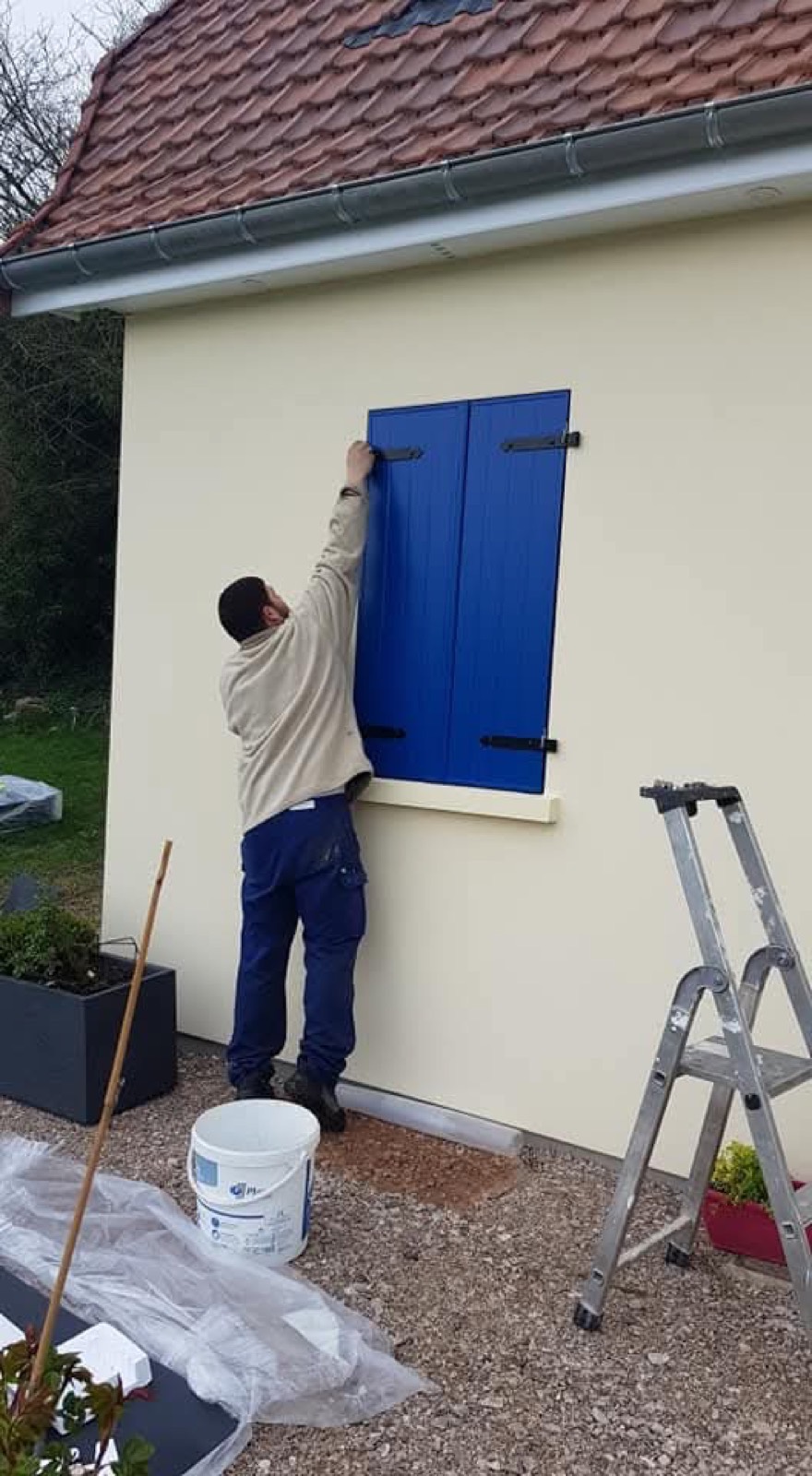Poseur Dagicour fixant un volet battant bleu sur une maison en Seine-Maritime